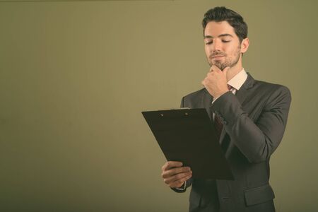 Young handsome businessman wearing suit against colored background