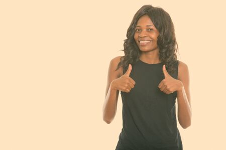 Studio shot of young happy black African woman smiling while giving thumbs upの写真素材