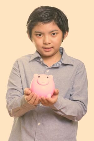 Studio shot of cute Japanese boy holding piggy bankの写真素材