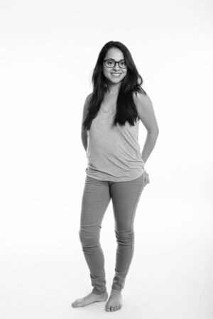 Full body shot of happy beautiful woman smiling and standing while wearing eyeglasses against white backgroundの写真素材