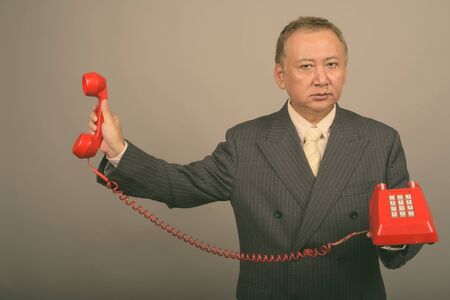 Portrait of mature Asian businessman with old telephone