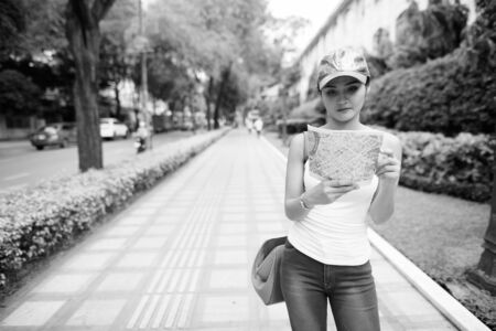 Young beautiful Asian tourist woman looking at the map in the city streets