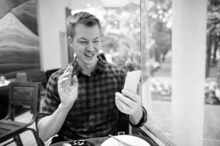 Happy young handsome tourist man vlogging with phone by the windowの写真素材