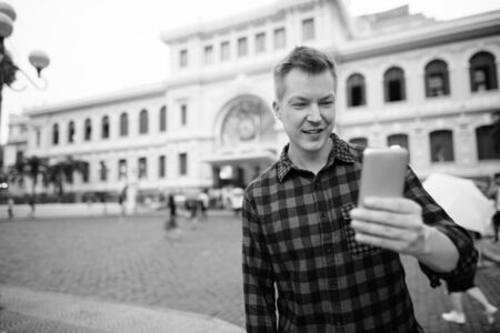 Happy young handsome tourist man using phone against historical building
