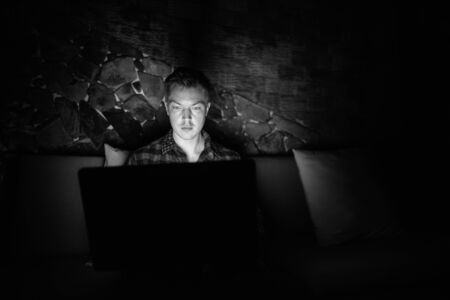 Young handsome man using laptop in the dark living room