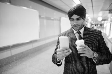 Young handsome Indian Sikh businessman using phone in subway station