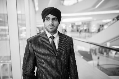 Young handsome Indian Sikh businessman looking through window