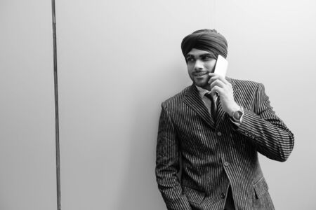 Happy young handsome Indian Sikh businessman talking on the phone