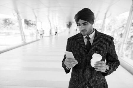 Young handsome Indian Sikh businessman using phone at the footbridgeの写真素材