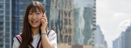 Happy young beautiful Asian teenage girl talking on the phone against view of the cityの写真素材