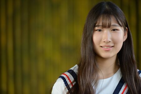 Happy young beautiful Asian teenage girl against bamboo fenceの写真素材