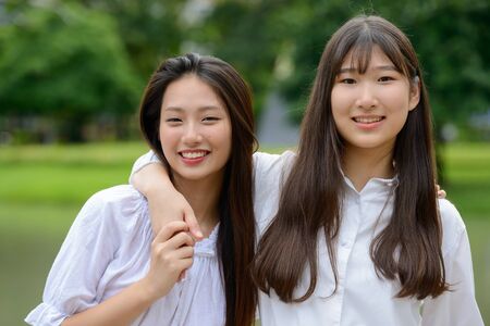 Two happy young beautiful Asian teenage girls bonding together at the park