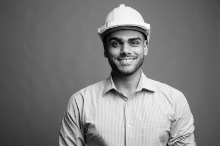 Young handsome Indian businessman as engineer against gray backgroundの写真素材
