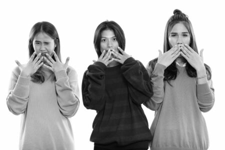 Studio shot of three young Asian woman friends covering mouth while looking shocked togetherの写真素材
