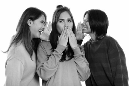Studio shot of young Asian woman looking shocked with both friends whispering on each sideの写真素材