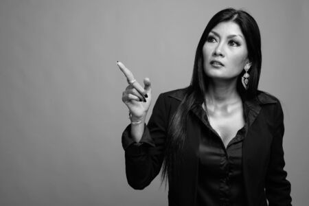 Mature beautiful Asian businesswoman against gray background