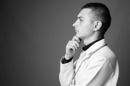 Portrait of young handsome man doctor against gray backgroundの写真素材