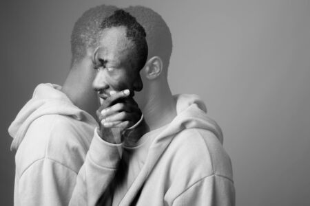 Studio shot of young African man wearing hoodie against gray background in black and whiteの写真素材