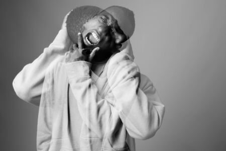Studio shot of young African man wearing hoodie against gray background in black and white