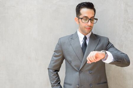 Young handsome Persian businessman checking the time against concrete wall outdoorsの写真素材
