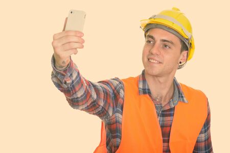 Happy young man construction worker smiling while taking selfie picture with mobile phoneの写真素材