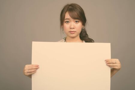 Young beautiful Asian tourist woman ready for vacation against gray background