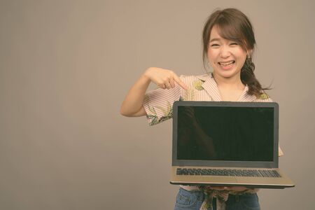 Young beautiful Asian tourist woman ready for vacation against gray backgroundの写真素材