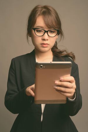 Young beautiful Asian businesswoman against gray backgroundの写真素材