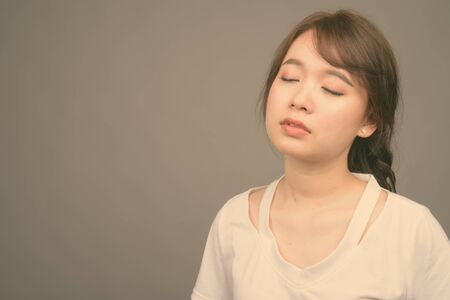 Young beautiful Asian woman against gray background