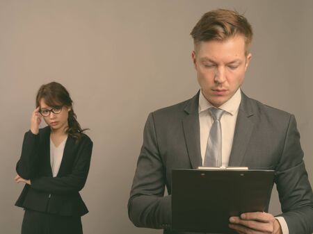 Young businessman and young Asian businesswoman against gray background