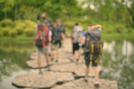 Defocused Portrait Of Blurred Tourist Backpackers Crossing The Lake In The Park