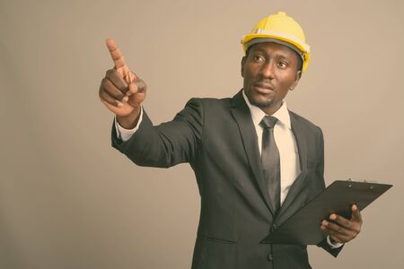 Young handsome African businessman with hardhat against gray background