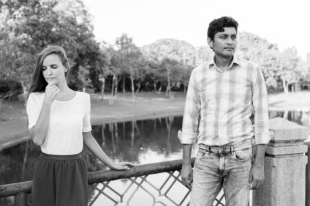 Multi ethnic couple thinking while looking sad on the bridge of peaceful green park