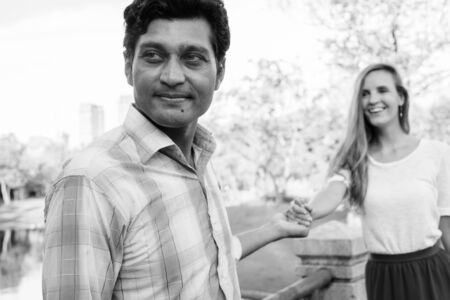 Close up of happy multi ethnic couple holding hands together on the bridge at the park