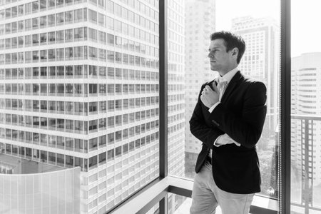 Young handsome businessman standing against glass window with view of the city