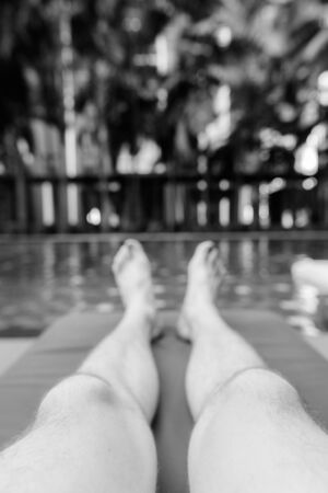 Feet of young handsome man relaxing by swimming pool in hotelの写真素材