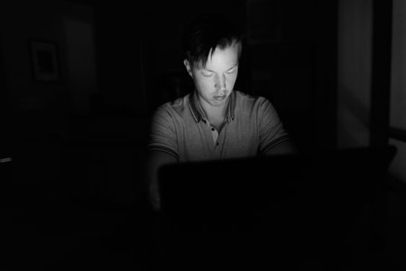 Young handsome man using laptop in the dark living room