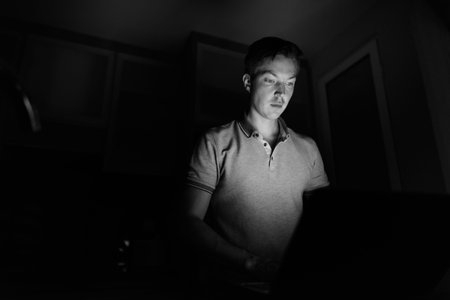 Young handsome man using laptop in the dark living room