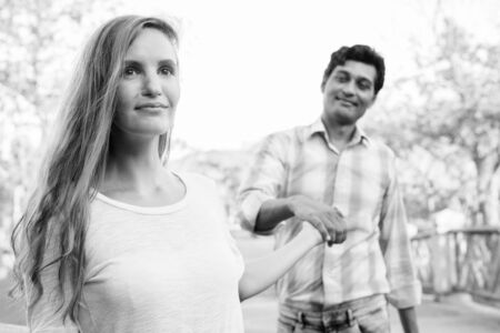 Close up of happy multi ethnic couple holding hands together on the bridge at the parkの写真素材