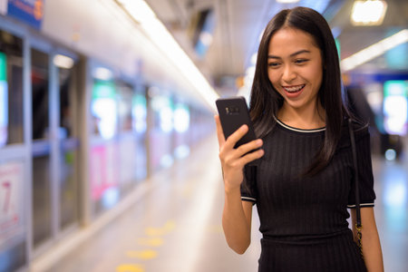 Happy young beautiful Asian tourist woman using phone at the subway stationの写真素材