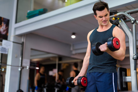 Young handsome man exercising with dumbbells at the gym