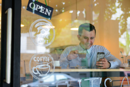 Happy young handsome businessman using phone at the coffee shop