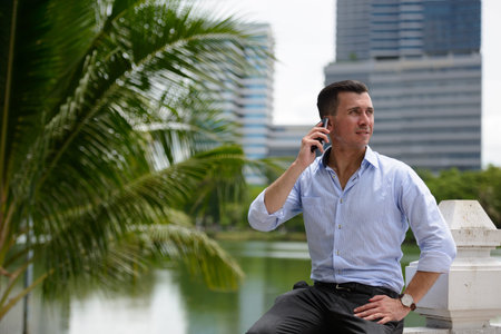 Young handsome businessman talking on the phone at the park