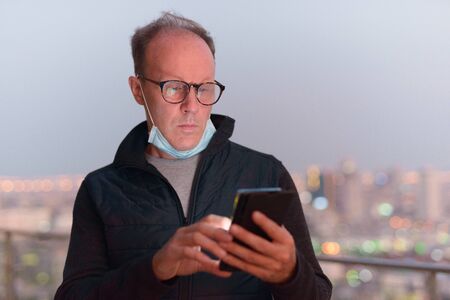 Mature man with mask using phone against view of the cityの写真素材