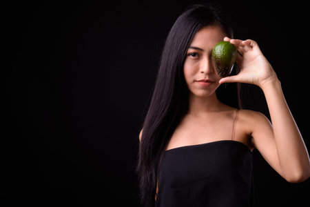 Portrait of young Asian woman holding avocado near face