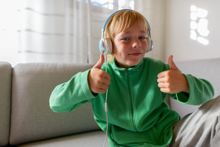 Happy young handsome boy listening to music and giving thumbs up at home
