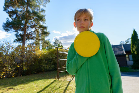 Young handsome boy thinking while holding flying disc in the front yardの写真素材