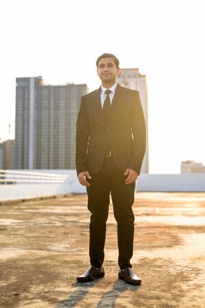 Full body shot of young Persian businessman in suit thinking against view of the cityの写真素材