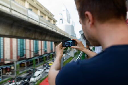 Closeup rear view of young man taking picture of the city streets with phoneの写真素材