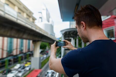 Closeup rear view of young man taking picture of the city using phoneの写真素材